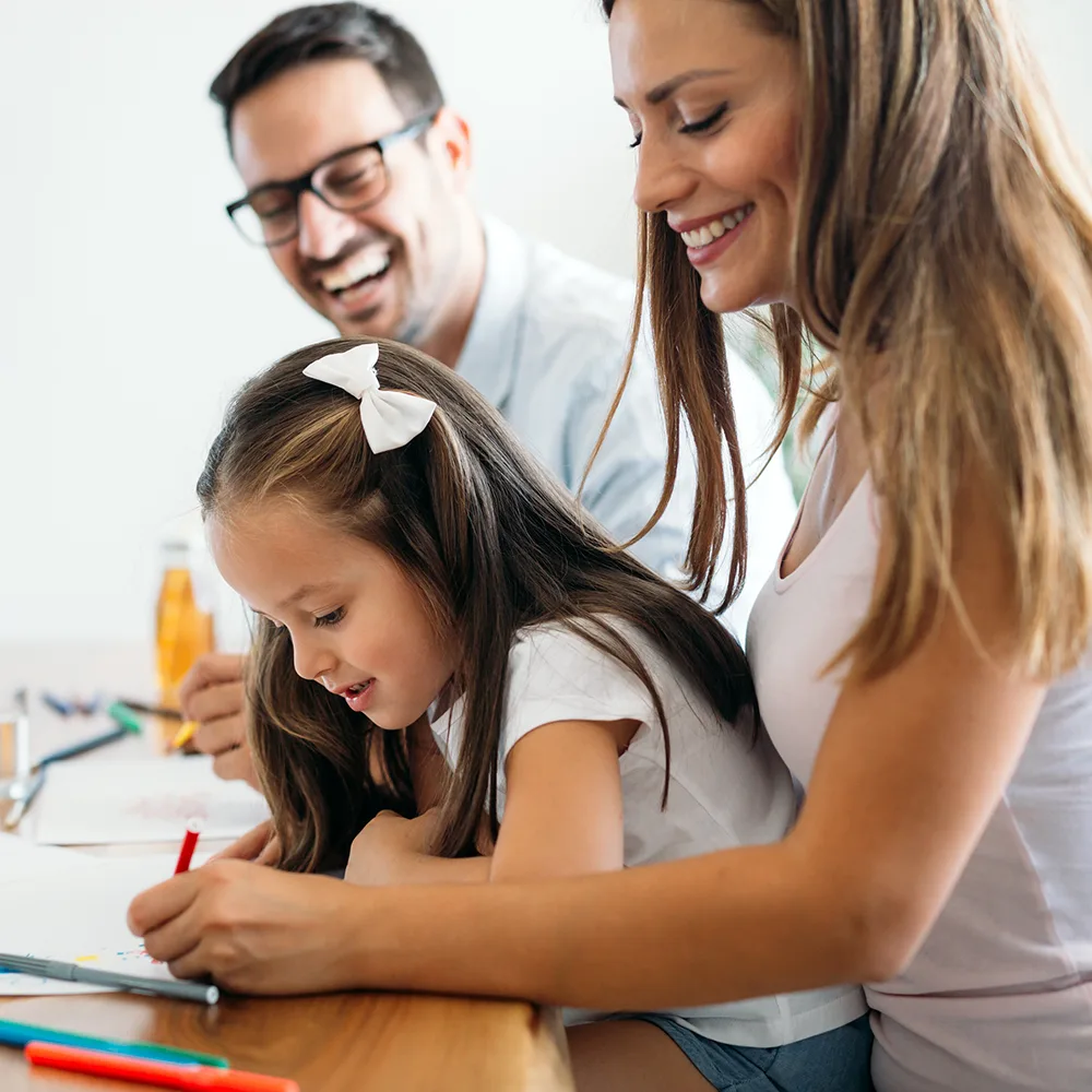 A laughing mother and father helping their child write in a book at a Bright Beginnings Academy daycare