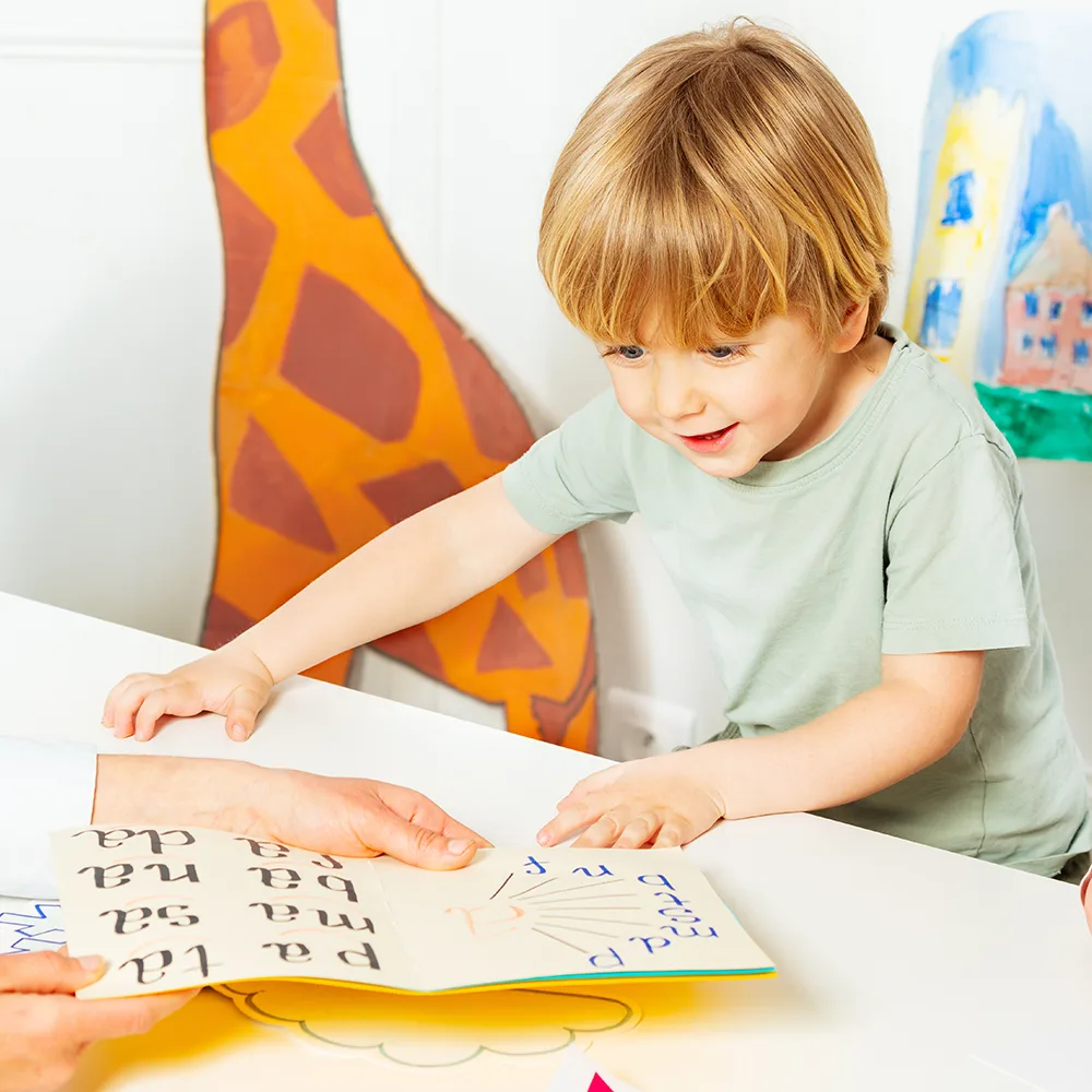 A child smiling and looking at a school book at a Bright Beginnings Academy daycare