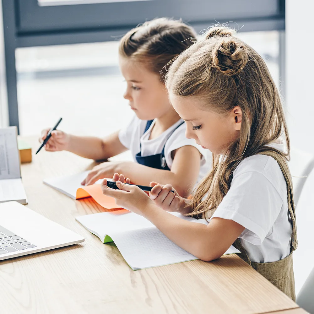 Two children working with pens and a laptop at a table in a Bright Beginnings Academy daycare