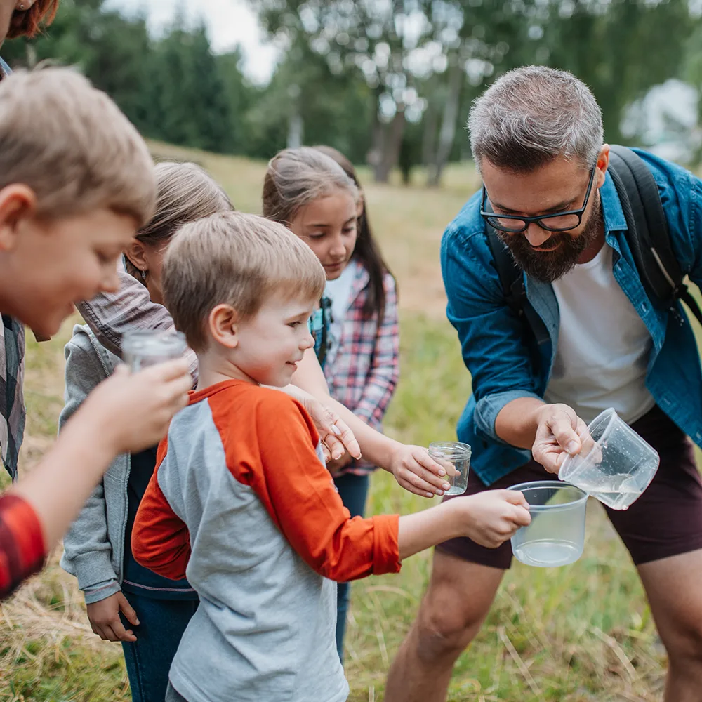 An adult playing with kids and glasses of water outside of a Bright Beginnings Academy daycare
