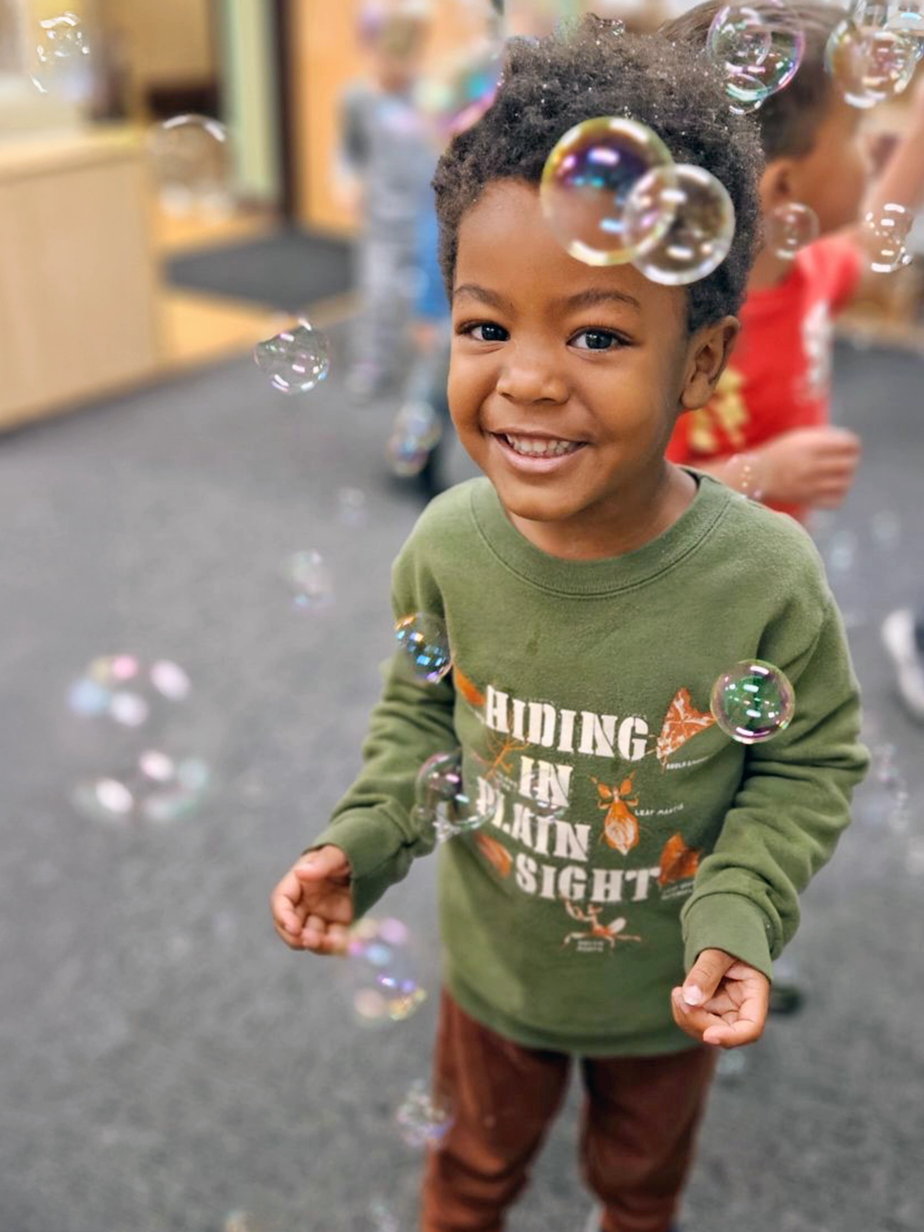 Child standing among floating bubbles at a Bright Beginnings Academy daycare.